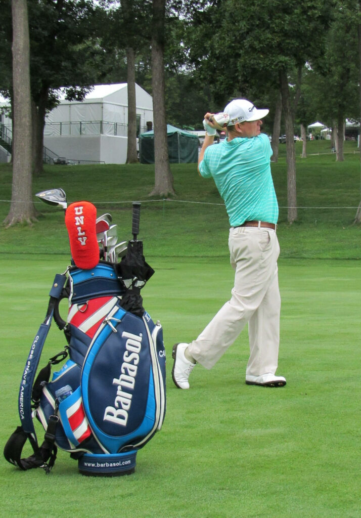 Chad Campbell mid golf swing on lush course with Barbasol golf bag turquoise shirt beige pants Wallpaper