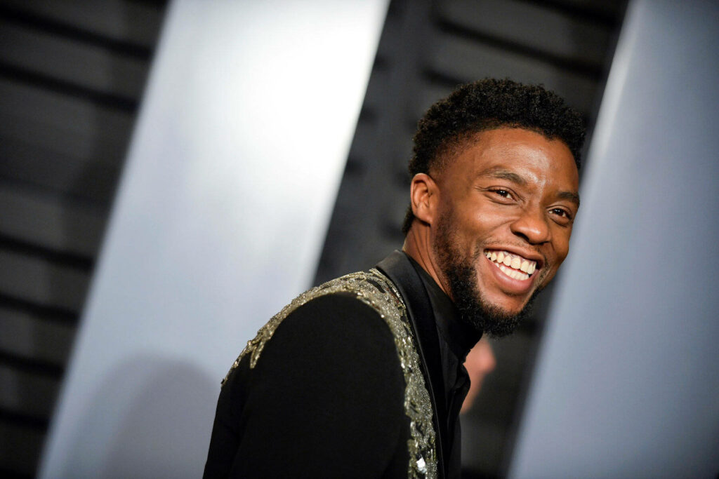 Chadwick Boseman smiling in stylish black jacket with shimmering details wallpaper background