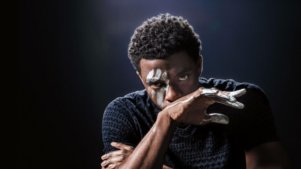 Chadwick Boseman intense gaze with bold white face and hand paint on dark cinematic background Wallpaper