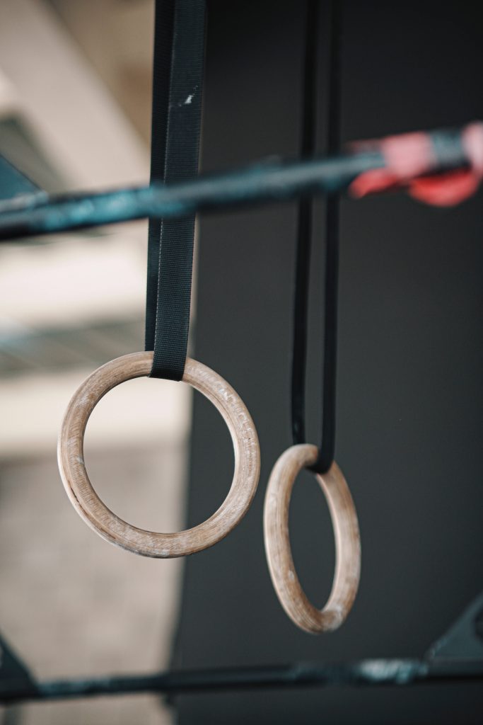 Chalk-dusted wooden gymnastics rings hanging on black straps in moody gym background wallpaper