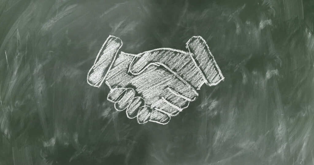 Handshake drawn in white chalk on green chalkboard symbolizing teamwork and partnership wallpaper