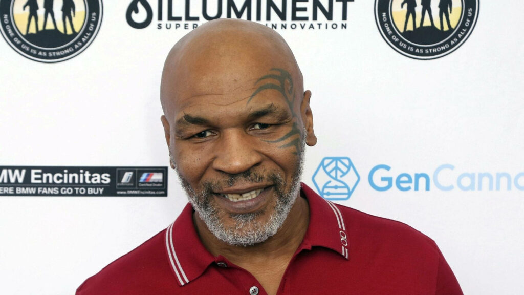 Powerful Presence: Smiling Mike Tyson Radiates Confidence in Front of Promotional Banner Wallpaper
