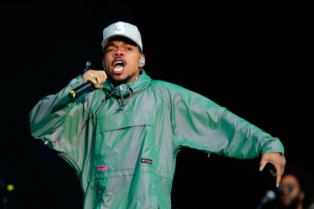 Chance The Rapper performing in green jumpsuit and grey hat dynamic stage shot dark background Wallpaper