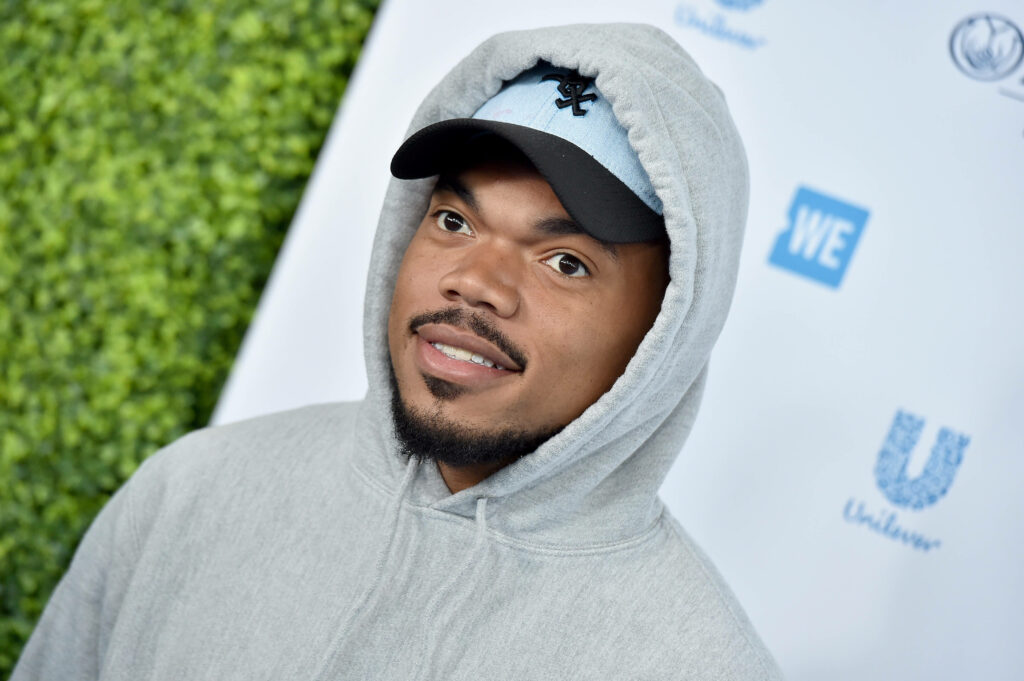 Chance The Rapper in light gray hoodie and black cap outdoors with green foliage background Wallpaper