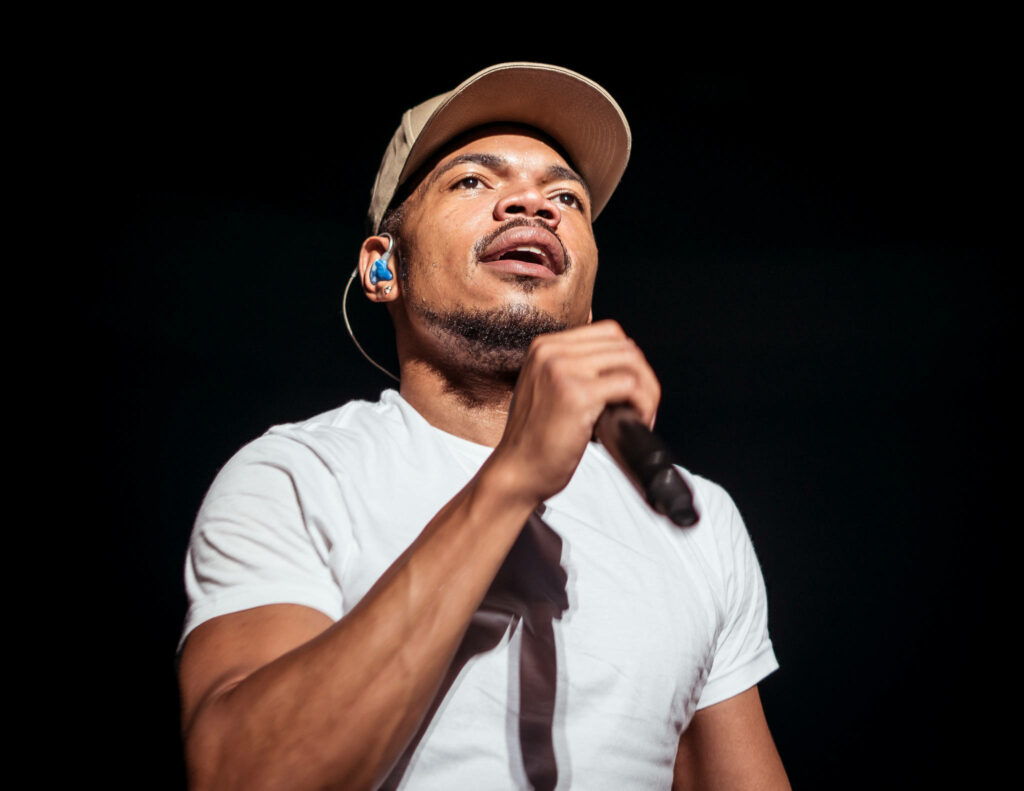 Chance The Rapper performing live in white t-shirt and tan cap with dramatic stage lighting Wallpaper