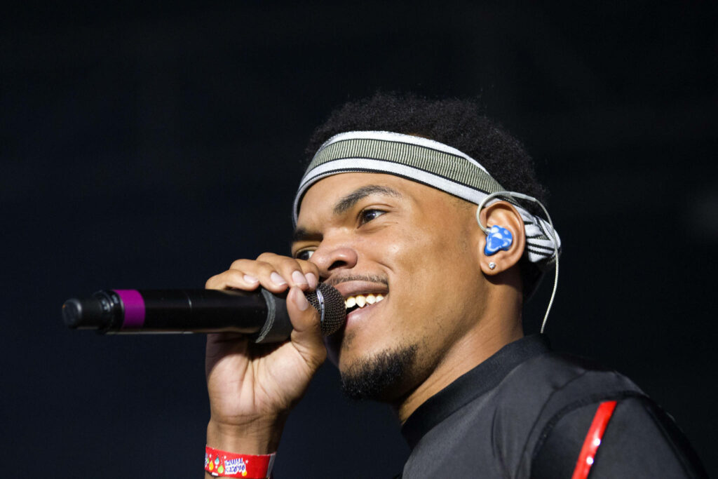 Chance The Rapper singing on stage wearing striped headband black outfit red accents vibrant energy Wallpaper