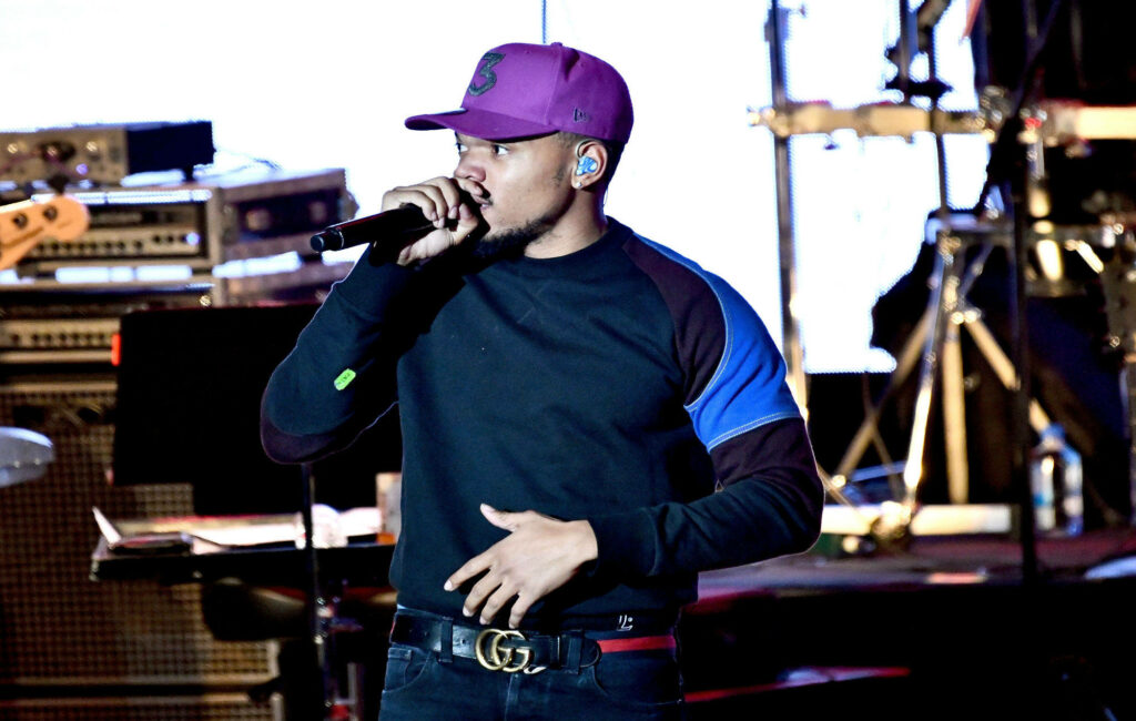 Chance The Rapper performing live on stage wearing purple cap and colorful sweater vibrant lighting Wallpaper