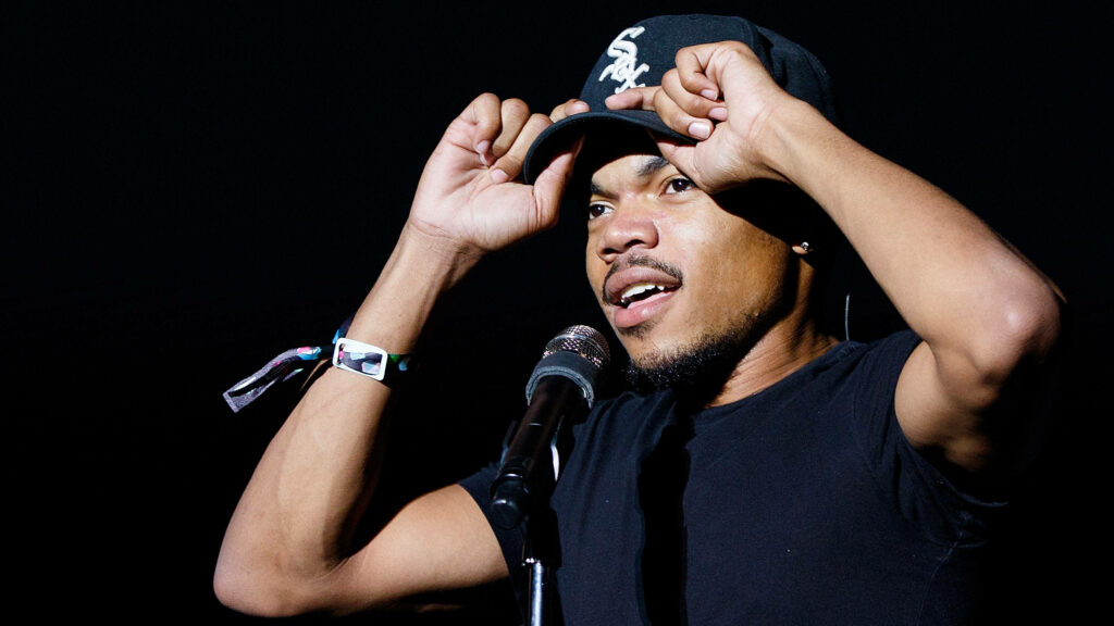 Chance The Rapper performing energetically with Chicago White Sox cap under spotlight Wallpaper