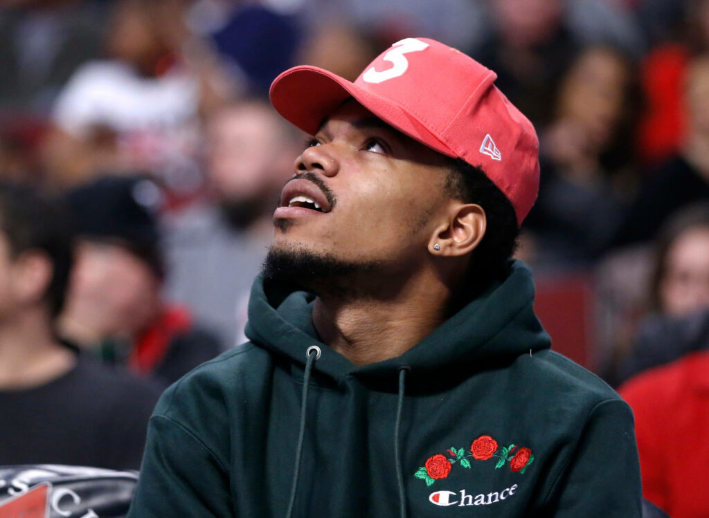 Chance The Rapper in pink cap and rose hoodie gazing upward at lively concert crowd wallpaper