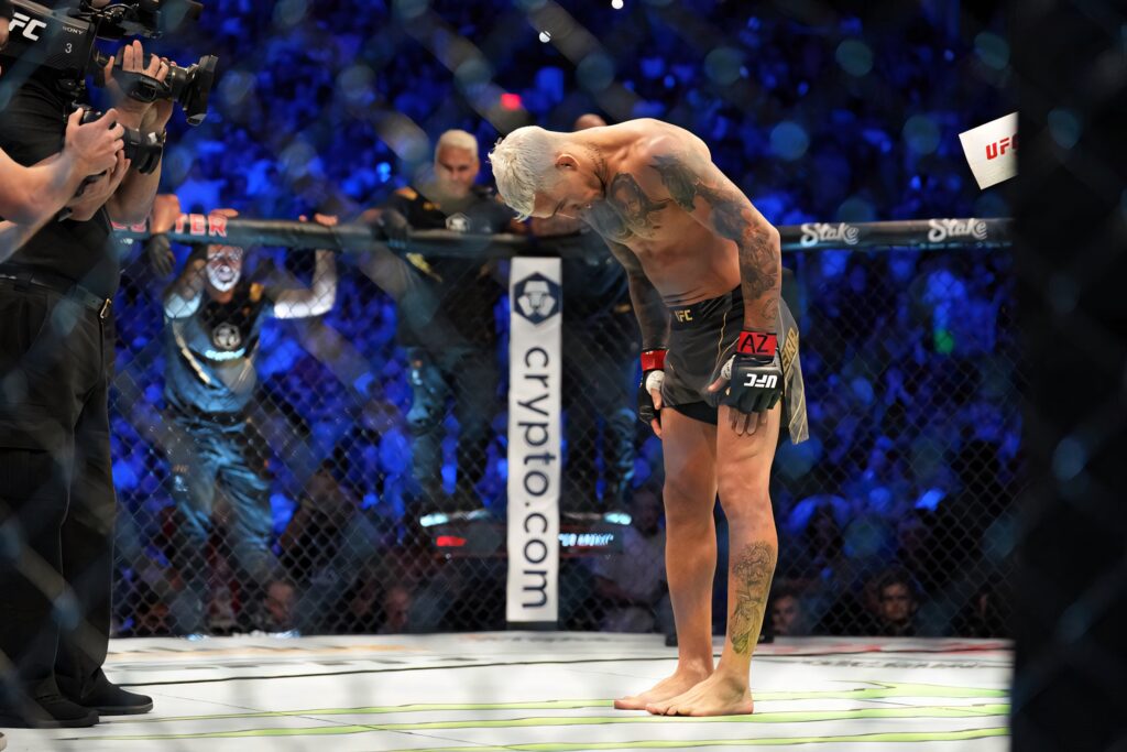 Charles Oliveira celebrating UFC victory inside octagon with vibrant blue lights and cheering crowd Wallpaper