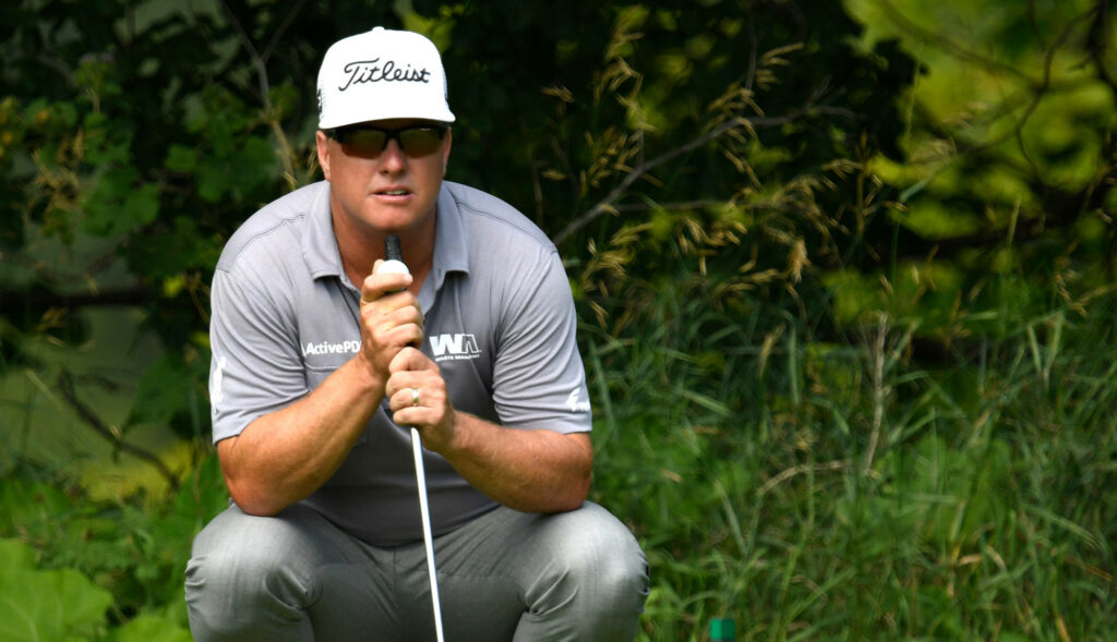 Charley Hoffman squatting on golf course focused in gray shirt white cap with lush green background Wallpaper