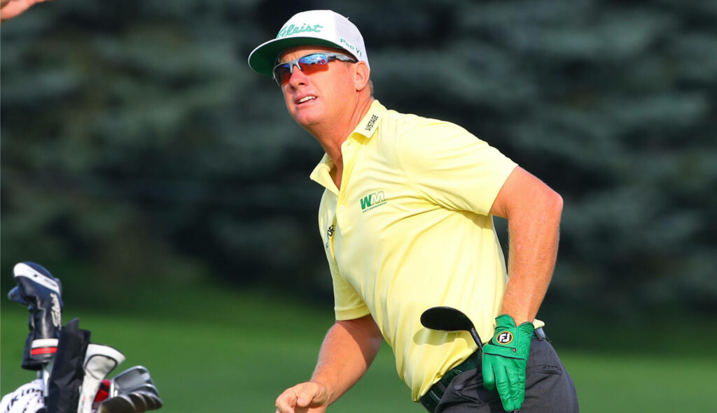 Charley Hoffman focused mid-game on sunny golf course wearing yellow shirt green glove white cap golf clubs nearby Wallpaper