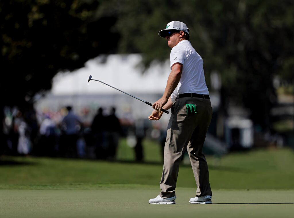 Charley Hoffman in classic golf attire focused on shot on vibrant green golf course in sunlight Wallpaper