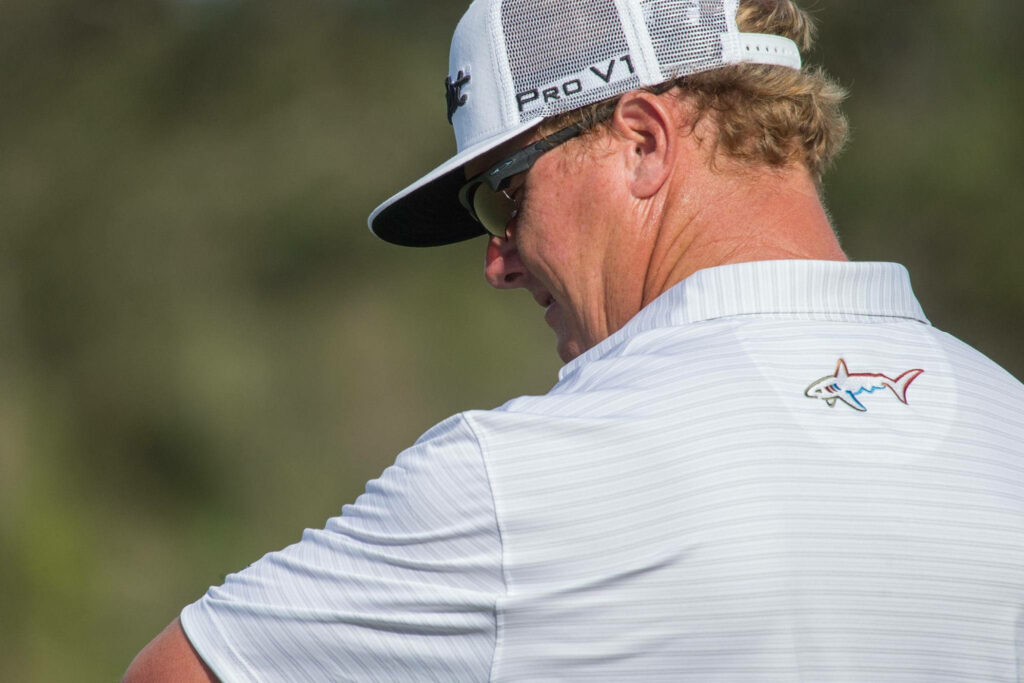 Back view of Charley Hoffman golf wallpaper with white cap colorful shark logo on green course