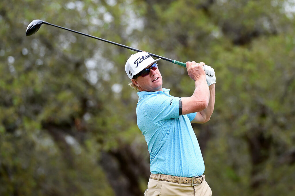 Charley Hoffman mid-swing on lush golf course wearing light blue polo and khaki pants focused Wallpaper