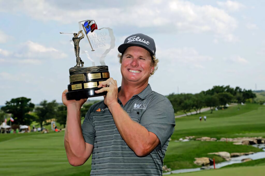 Charley Hoffman holding Valero Texas Open trophy on vibrant golf course under bright sky Wallpaper