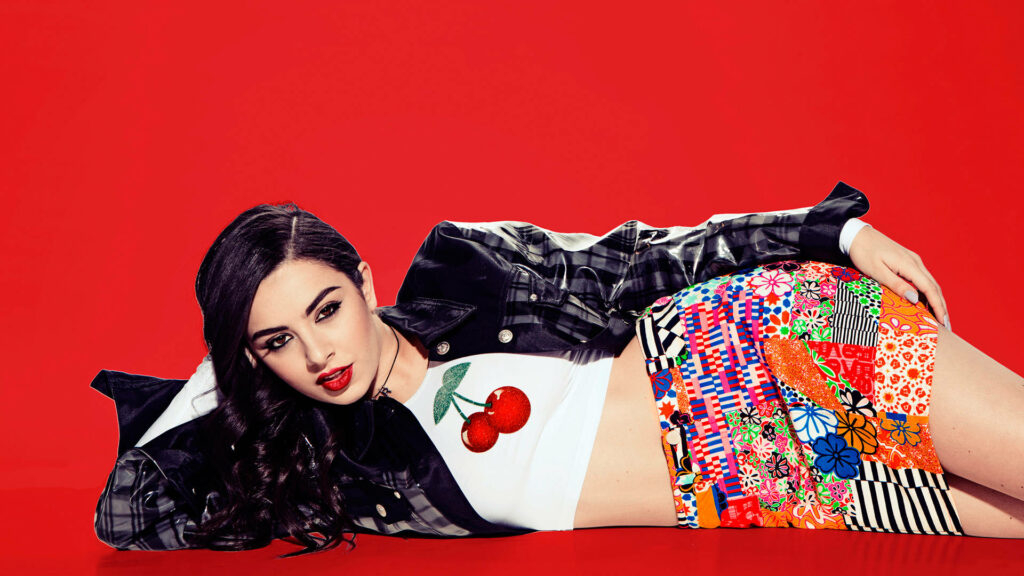 Charli XCX stylish in patterned skirt white cherry top black jacket bold red background wallpaper