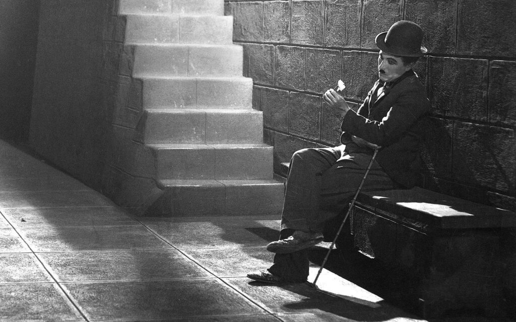 Charlie Chaplin sad reflective portrait sitting alone on bench black and white wallpaper background