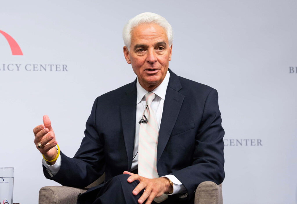 Charlie Crist in dark suit white shirt striped tie seated in professional formal setting wallpaper