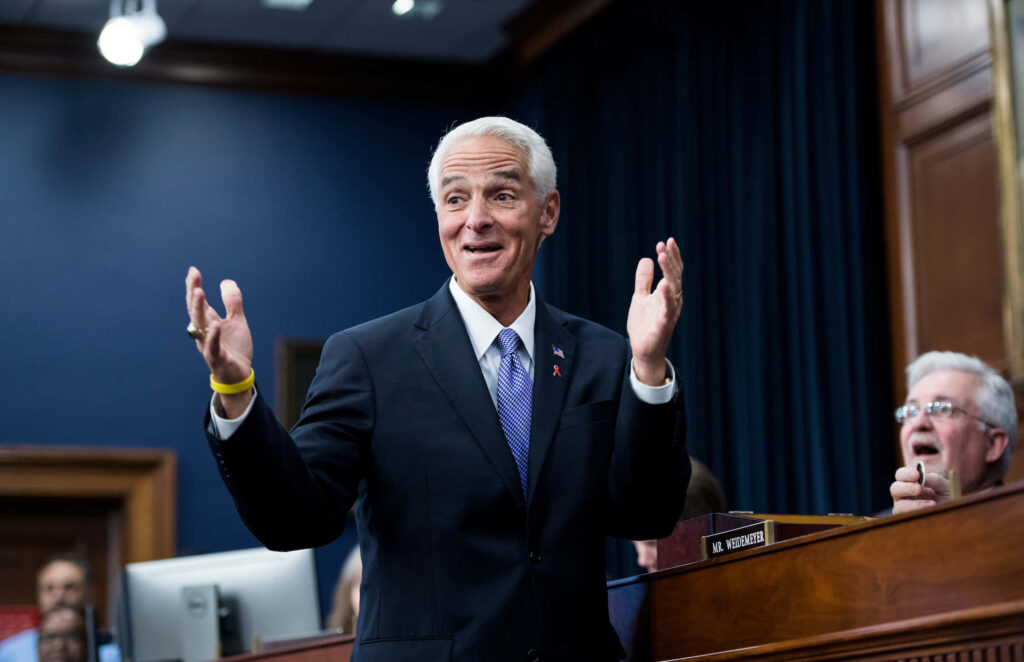 Charlie Crist in dark suit raising hands in formal setting with wood paneling and officials Wallpaper