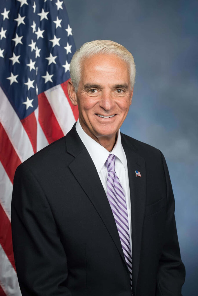 Charlie Crist in black suit and purple striped tie in front of American flag formal portrait Wallpaper