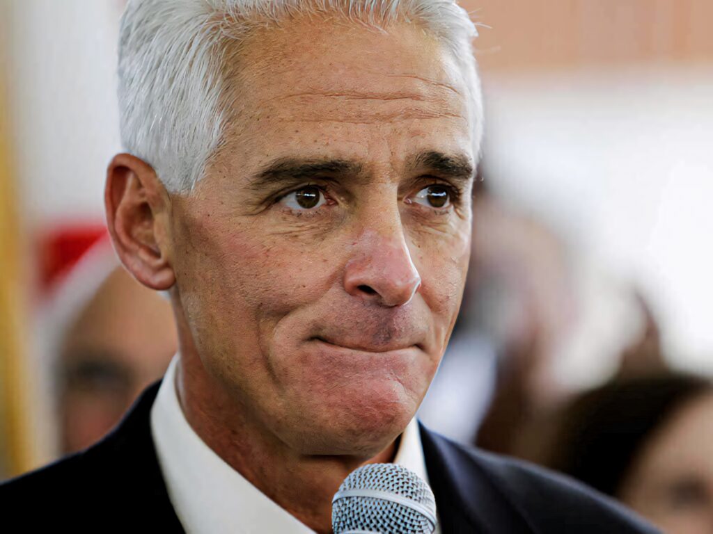 Charlie Crist holding microphone with thoughtful expression in formal attire and blurred background Wallpaper