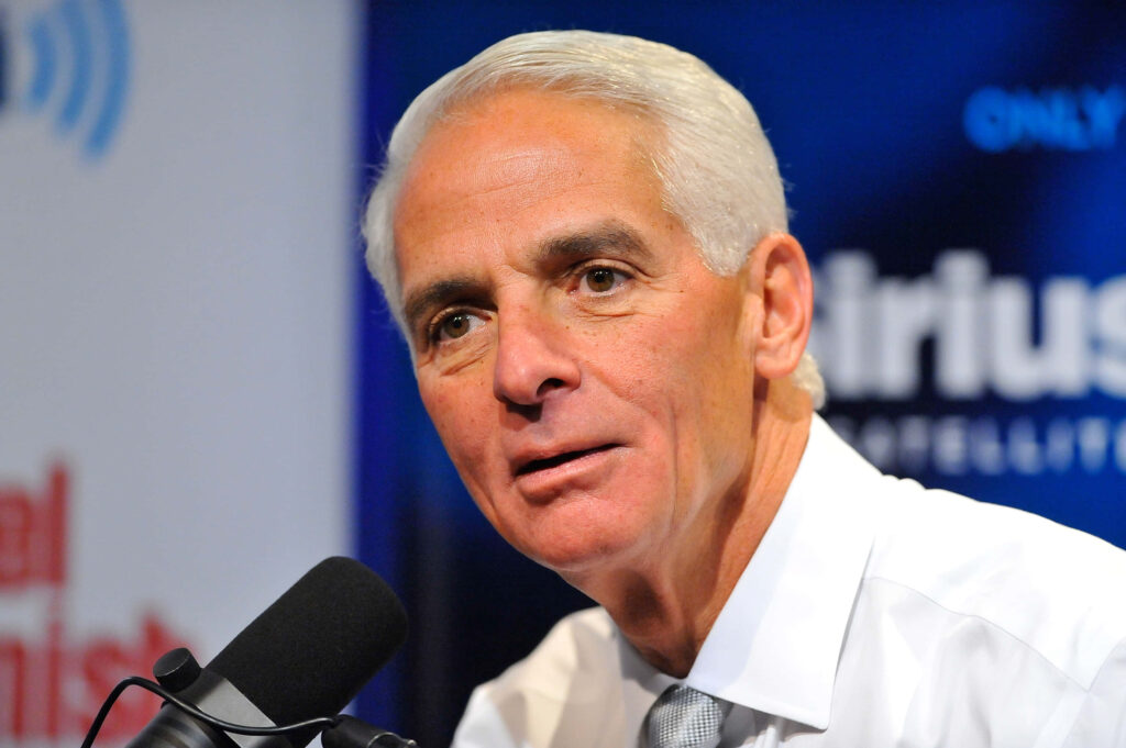 Charlie Crist speaking into microphone in blue studio during radio interview professional wallpaper background
