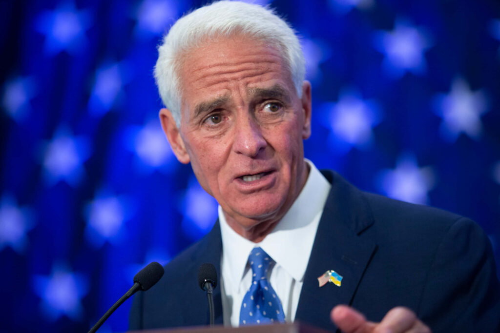 Charlie Crist speaking at podium in dark suit with blue starry background political wallpaper