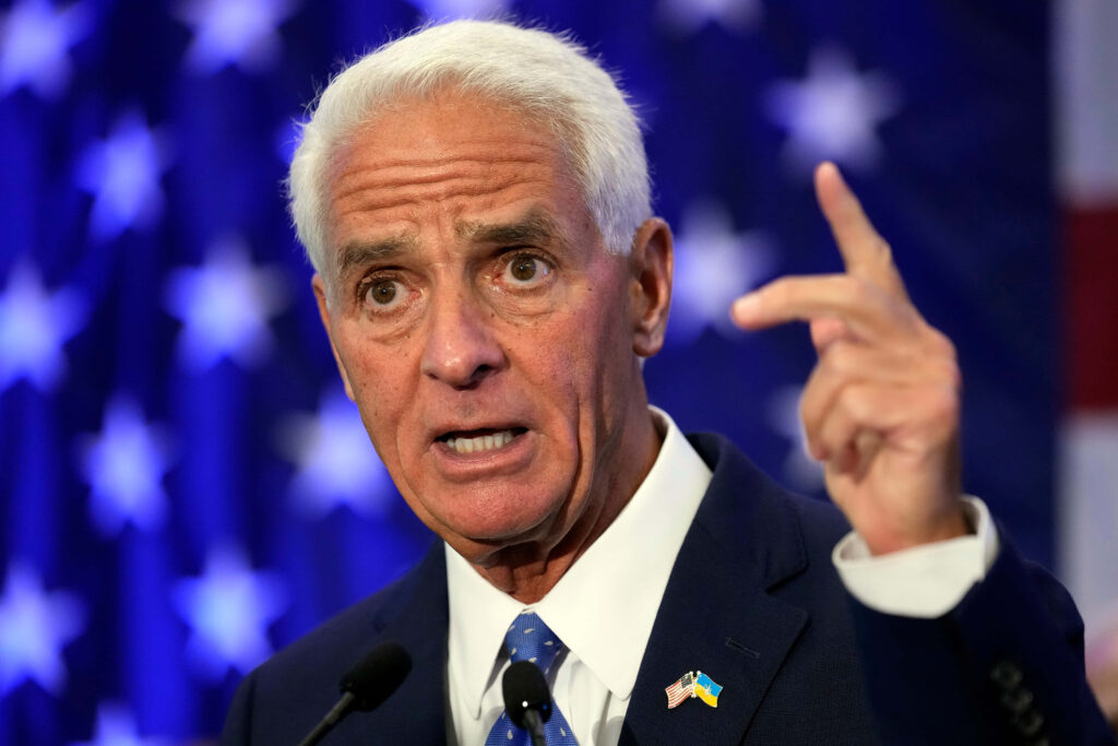 Charlie Crist speaking with signature hand gesture American flag stars backdrop vibrant colors Wallpaper