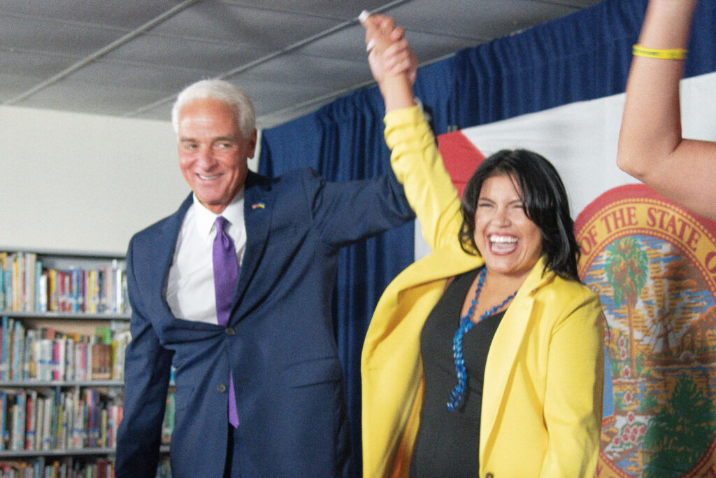Charlie Crist and Karla Hernandez-Mats celebrating united with Florida flag and bookshelf background Wallpaper