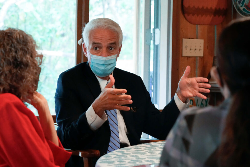 Charlie Crist wearing blue surgical mask and suit discussing health in bright indoor setting Wallpaper