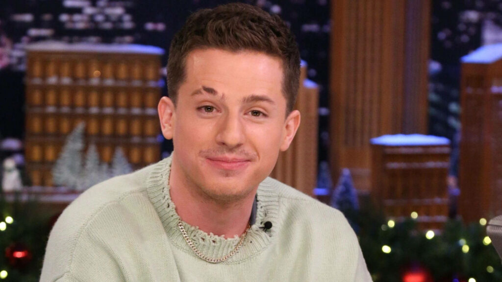 Charlie Puth smiling warmly in cozy winter setting with festive decorations and snow background Wallpaper