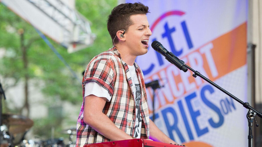 Charlie Puth singing live on stage with energetic concert atmosphere and vibrant wallpaper background