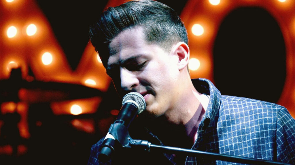 Charlie Puth singing passionately on dark stage with dramatic lighting wallpaper background