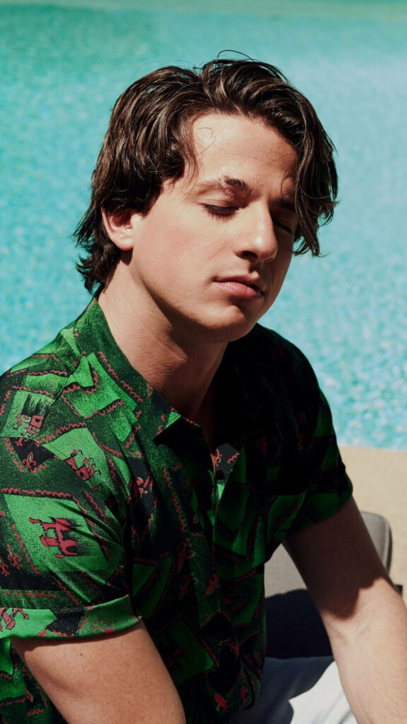 Charlie Puth relaxing with eyes closed enjoying sunlight by a sparkling blue pool wallpaper