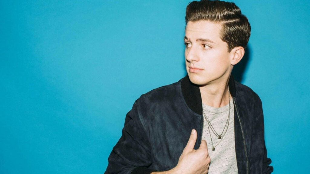 Charlie Puth looking sideways in casual grey shirt and dark jacket against vibrant blue background Wallpaper