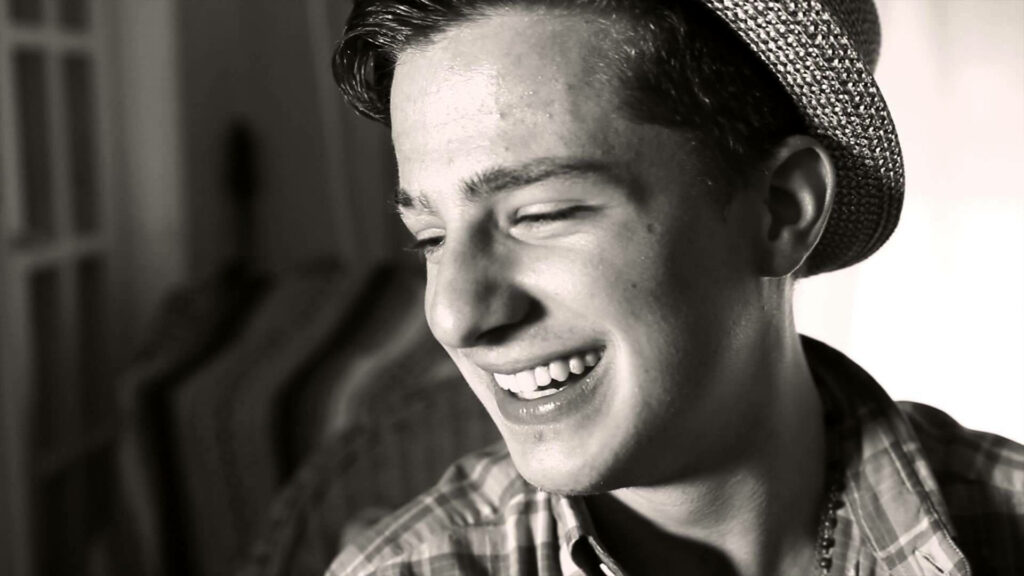 Charlie Puth smiling warmly in cheerful wallpaper background radiating joy and happiness