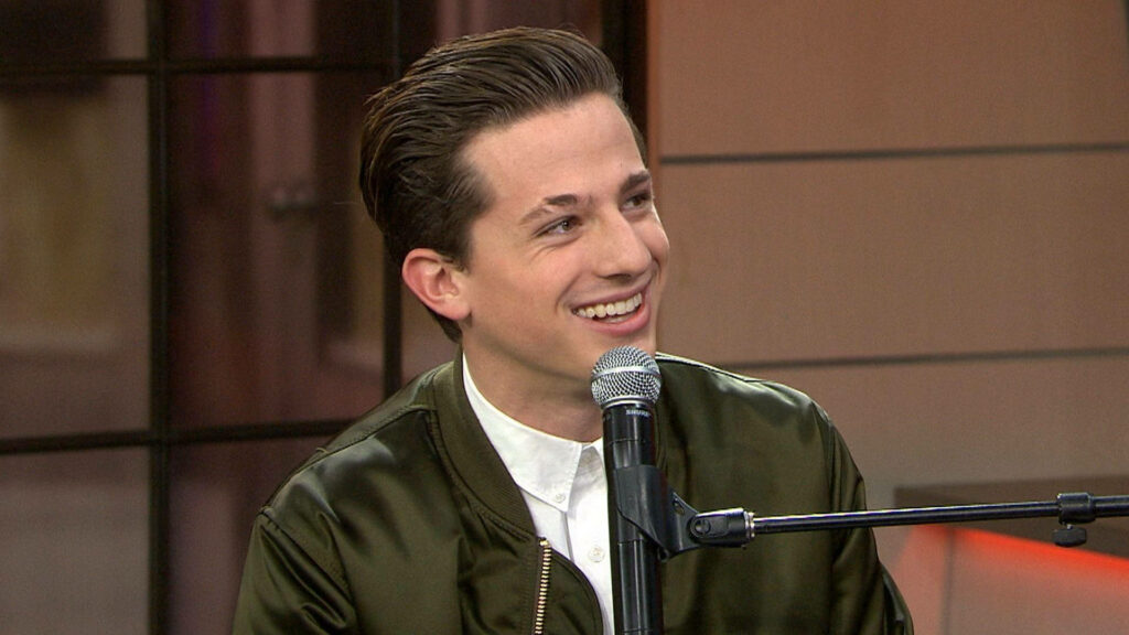 Charlie Puth smiling at piano wearing green jacket holding microphone lively wallpaper background