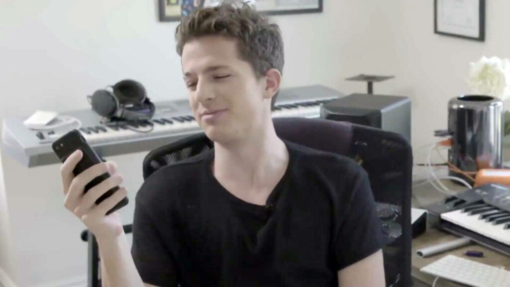Charlie Puth smiling in a music studio looking at cellphone with keyboards and audio gear background Wallpaper