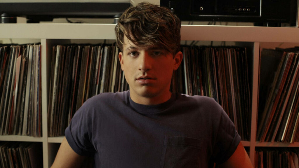 Charlie Puth calm and introspective sitting by vinyl records shelf wallpaper background