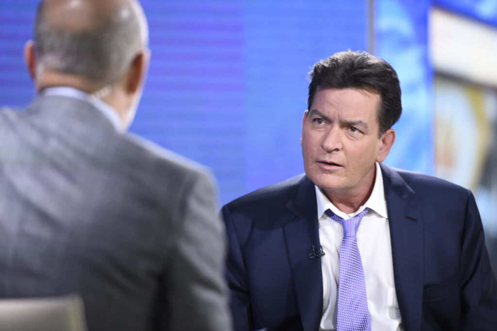 Charlie Sheen in navy suit and blue tie during candid TV interview with cool blue background Wallpaper