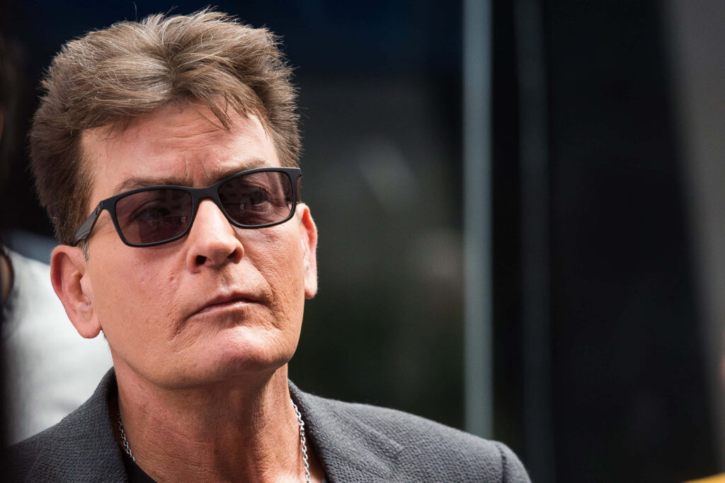Charlie Sheen close-up portrait wearing dark jacket and sunglasses with natural lighting wallpaper