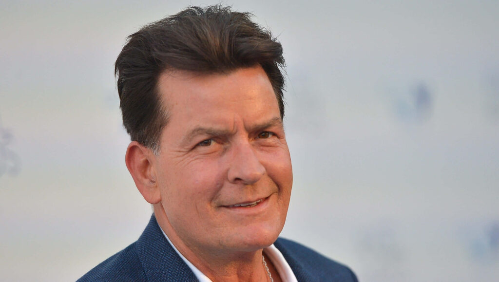 Charlie Sheen close-up portrait with relaxed smile soft lighting and muted blue suit wallpaper background