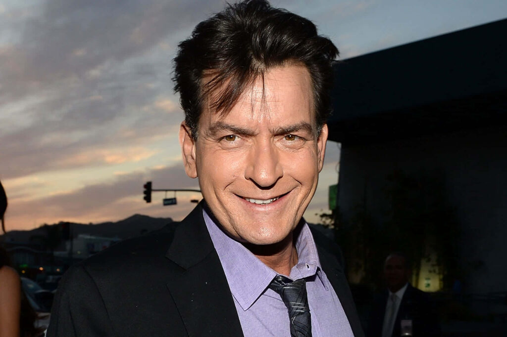 Charlie Sheen in black suit and purple shirt at sunset with warm light wallpaper background