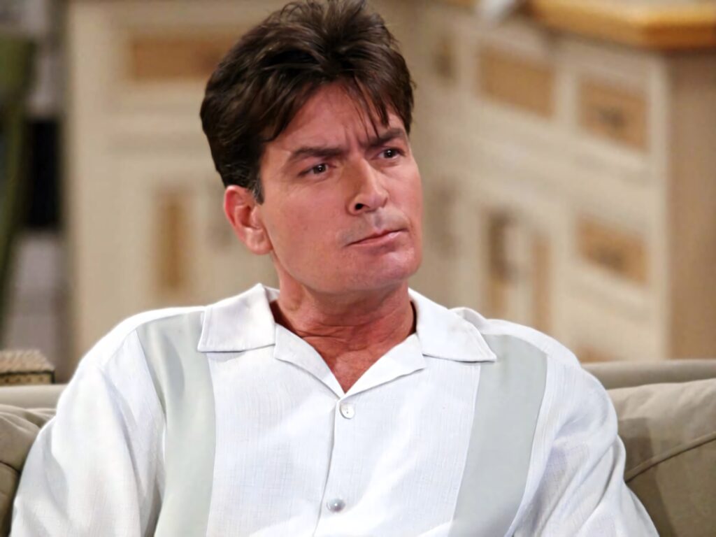 Charlie Sheen seated indoors in light collared shirt with thoughtful expression cozy sitcom setting Wallpaper