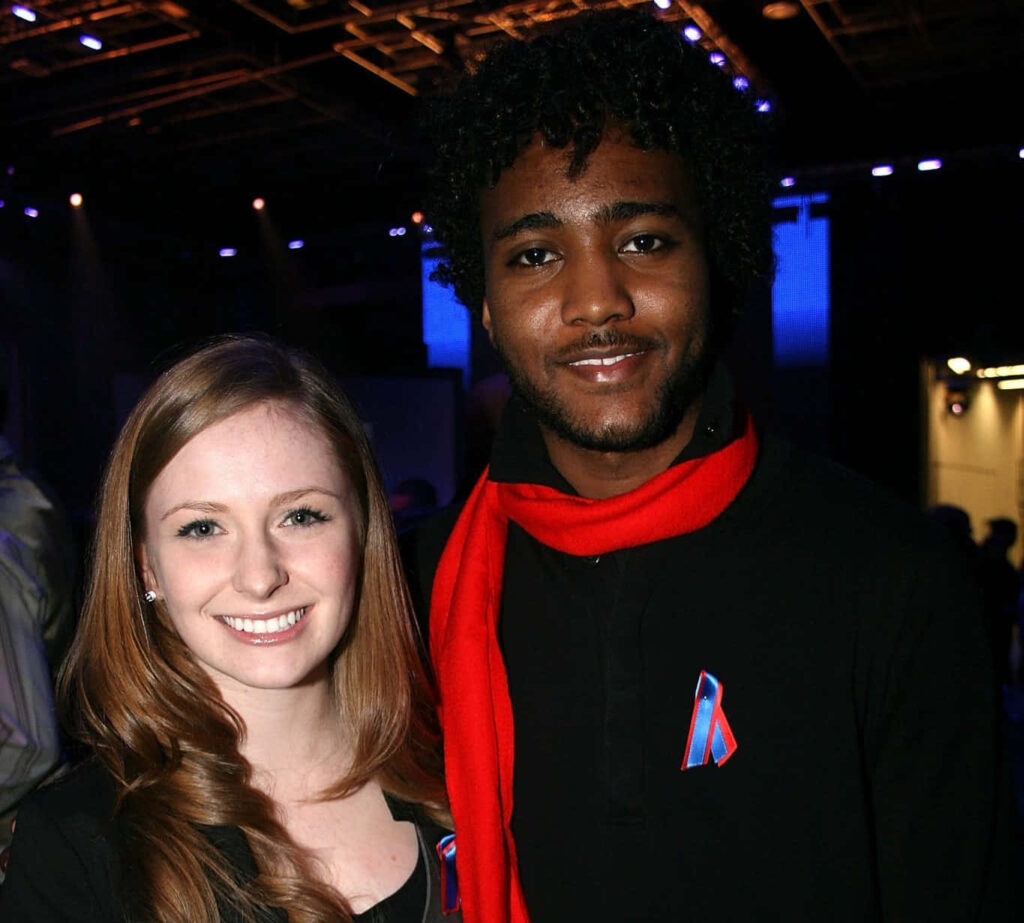 Charlotte Arnold and companion in dark outfits with ribbons at vibrant blue purple event background Wallpaper