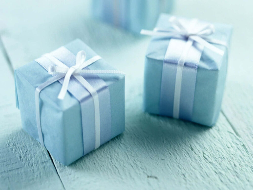 Two baby blue gift boxes with white ribbons on light wooden surface charming background wallpaper