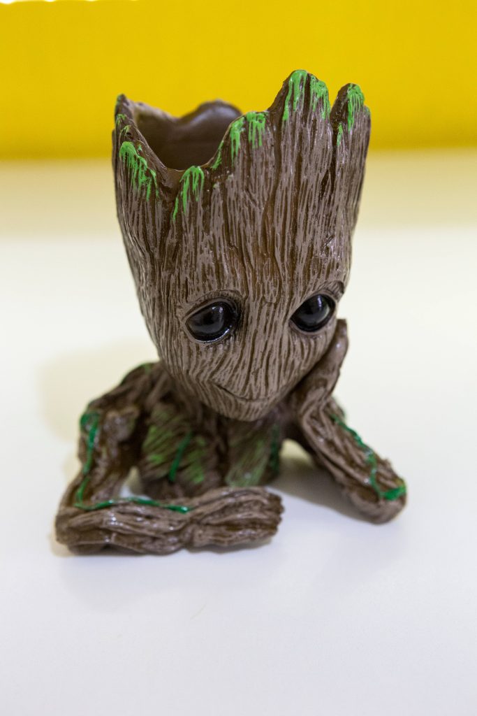 Close-up of Baby Groot planter figurine with detailed vines wood texture on yellow white backdrop Wallpaper