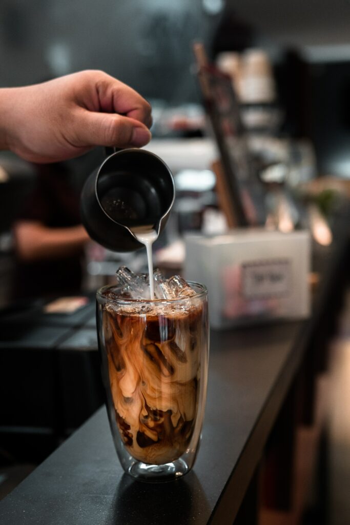 Refreshing Iced Coffee Preparation with Creamy Milk in Cozy Café Wallpaper