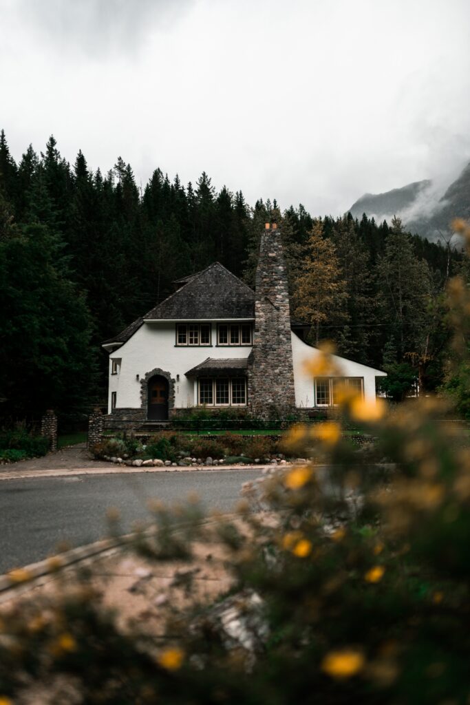Charming white house with tall stone chimney in lush green forest with mist and yellow flowers Wallpaper